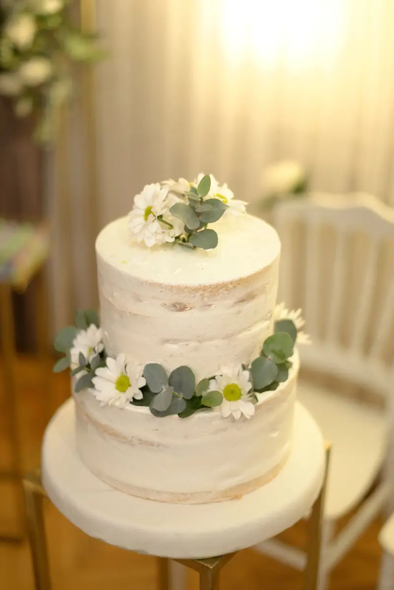 Hvit «naked cake» i to etasjer pyntet med hvite blomster og grønt